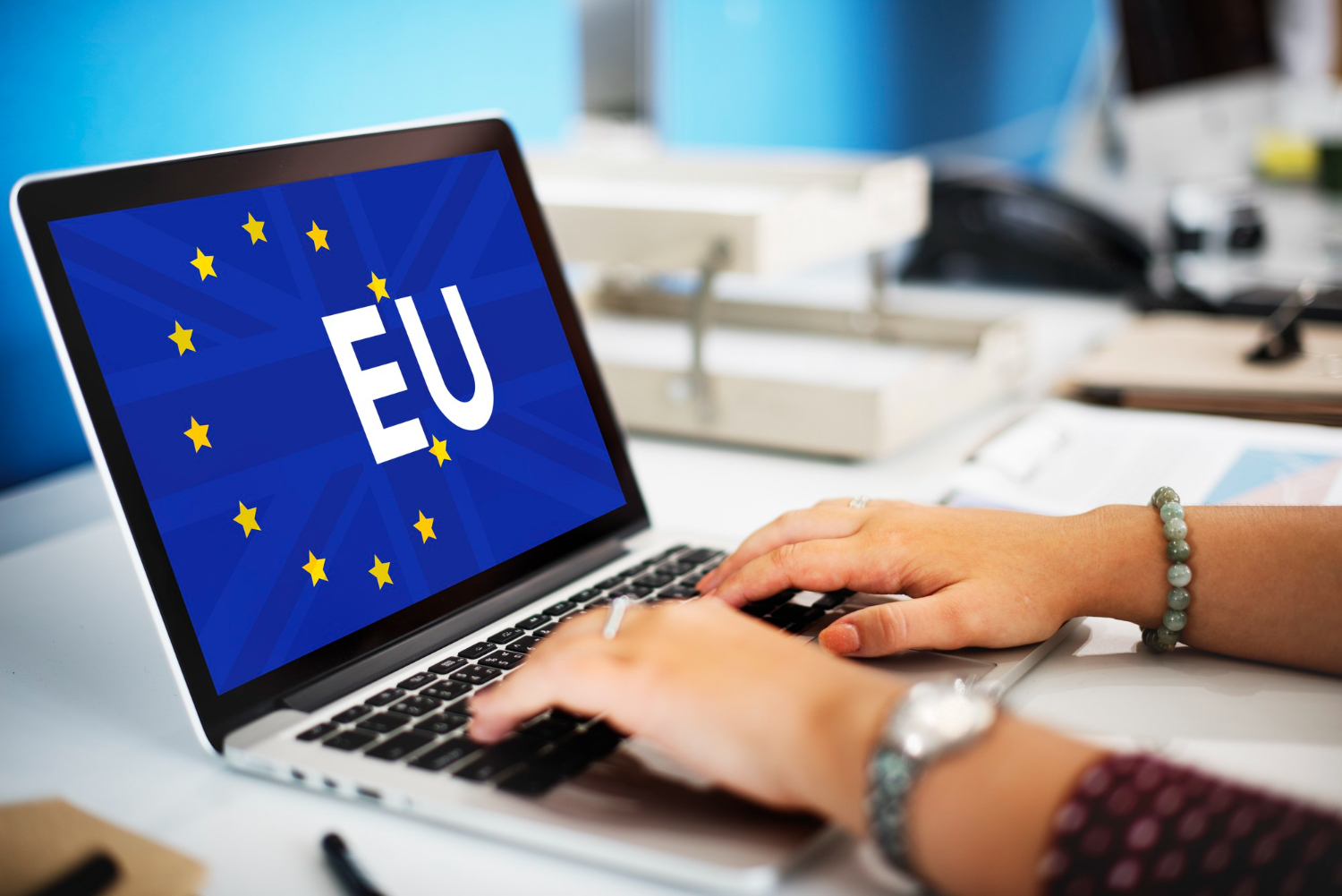 Person typing on laptop with EU flag in office setting